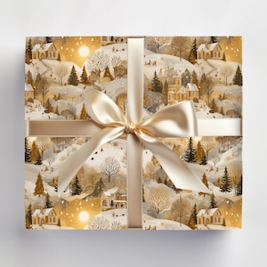 May include: A wrapped gift box featuring a winter landscape design with houses, trees, and a golden sun. The box is tied with a cream-colored satin ribbon and bow. The overall color scheme is gold, cream, and white.