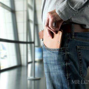 Pu&ograve; includere: Un portafoglio in pelle marrone &egrave; infilato nella tasca anteriore di un paio di jeans blu.