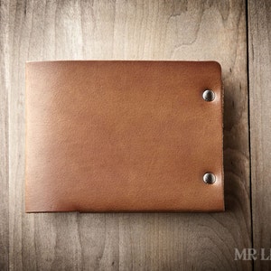 May include: A brown leather wallet with silver rivets. The wallet is closed and lying flat on a wooden surface.