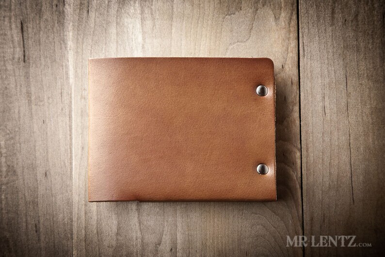 May include: A brown leather wallet with silver rivets. The wallet is closed and lying flat on a wooden surface.