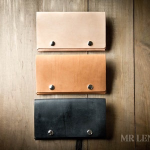 May include: Three leather wallets in different colors: light brown, tan, and black. Each wallet has two silver rivets on the front.