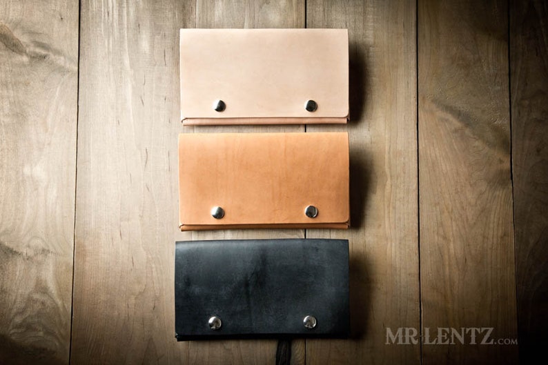 May include: Three leather wallets in different colors: light brown, tan, and black. Each wallet has two silver rivets on the front.