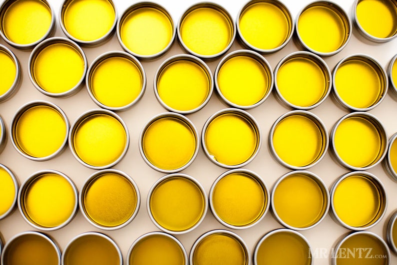 May include: A collection of small, round, yellow containers with silver lids. The containers are arranged in a grid pattern on a white surface.