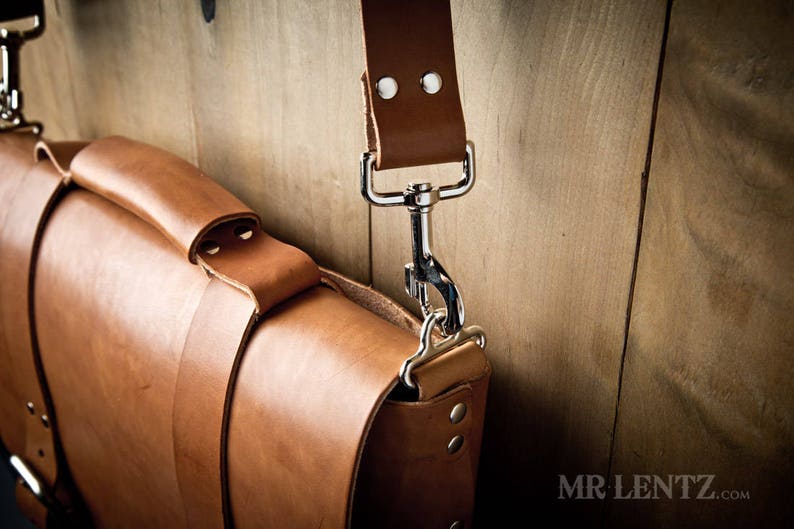 Pode incluir: Uma bolsa de mensageiro de couro marrom com um fecho de prata e uma al&ccedil;a. A bolsa &eacute; feita de couro de alta qualidade e tem um design cl&aacute;ssico.