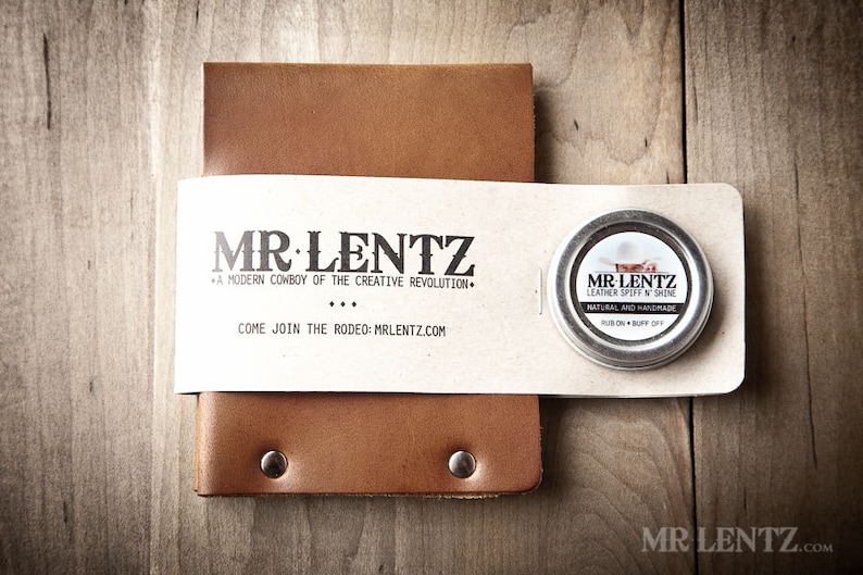 May include: A brown leather notebook with a small tin of leather polish. The tin has a label that says "MR LENTZ Leather Spoff N Shine" and "Natural and Handmade". The notebook has a label that says "MR LENTZ" and "A modern cowboy of the creative revolution".