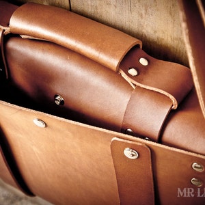 Pode incluir: Uma bolsa de couro marrom com fecho de aba e uma al&ccedil;a longa. A bolsa tem v&aacute;rios rebites de metal prateado e est&aacute; aberta para revelar o interior.