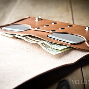 May include: A brown leather wallet with a flap that opens to reveal a cash compartment and two card slots. The wallet has silver rivets and a metal eyelet.
