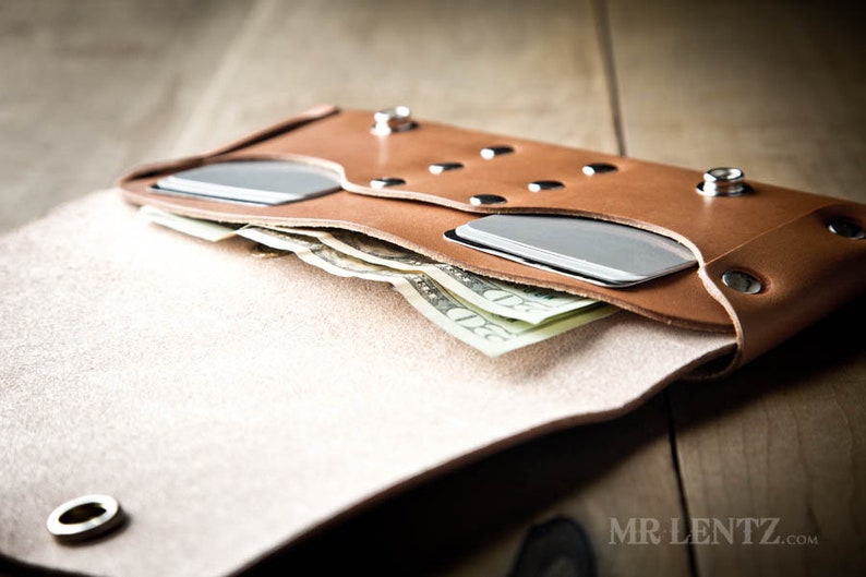 May include: A brown leather wallet with a flap that opens to reveal a cash compartment and two card slots. The wallet has silver rivets and a metal eyelet.