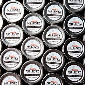 May include: A close-up view of multiple small silver tins, each containing a leather conditioner. The tins are arranged in a grid pattern and feature a white label with black text that reads "MR LENTZ LEATHER SPIFF 'N SHINE NATURAL AND HANDMADE RUB ON BUFF OFF".