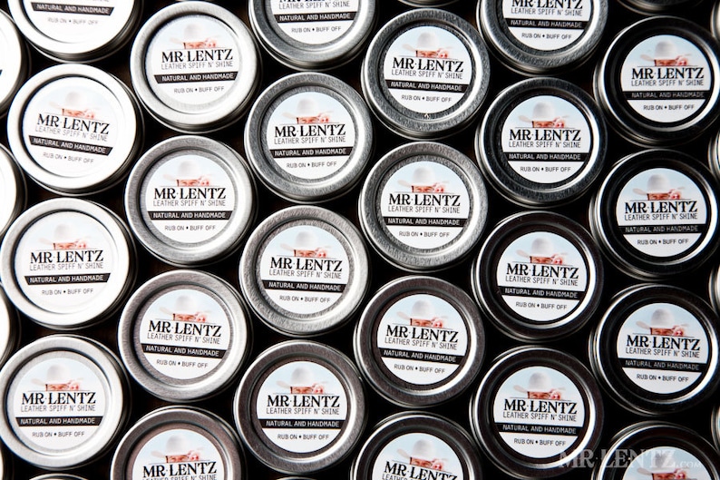 May include: A close-up view of multiple small silver tins, each containing a leather conditioner. The tins are arranged in a grid pattern and feature a white label with black text that reads "MR LENTZ LEATHER SPIFF 'N SHINE NATURAL AND HANDMADE RUB ON BUFF OFF".