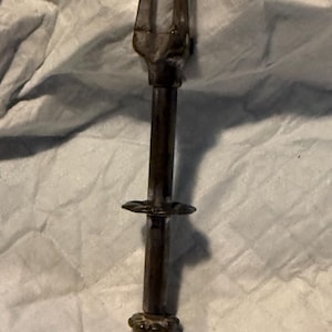 Puede incluir: Una pinza de servir de metal vintage con un acabado marrón oscuro. Las pinzas tienen un mango con una base decorativa y una sección media circular. La parte superior tiene un diseño curvo en forma de garra para agarrar alimentos.