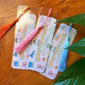 May include: Bookmarks with colorful tassels. Each bookmark features the text "Where you lead, I will follow" and illustrations of a building, a burger, and a coffee cup. The bookmarks are in clear plastic sleeves.