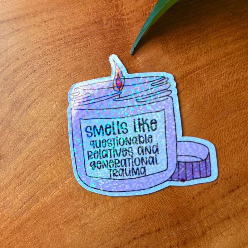 May include: A sticker in the shape of a candle jar with the text "Smells like questionable relatives and generational trauma." The candle is purple with a holographic effect, and the flame is red and orange.