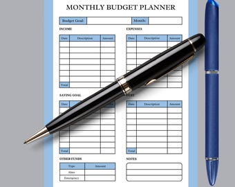 May include: A monthly budget planner with a light blue border, featuring sections for income, expenses, and savings. A black pen with silver accents and a blue pen are positioned on the planner.
