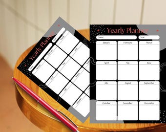 以下が含まれることがあります： 「Yearly Plan」の文字が入った白黒の年間プランナーシート2枚と、木製のテーブルに置かれた赤いペン。プランナーは、月がリストされたグリッドレイアウトになっています。ペンは赤色です。