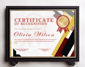 May include: Framed certificate of recognition with the text "Certificate of Recognition" and the name "Olivia Wilson." The certificate has a gold seal and red, black, and yellow geometric accents. The frame is black.