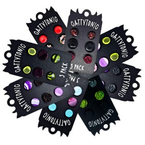 May include: A collection of stud earrings on black cards. Each card displays three earrings with various designs, including swirls, floral patterns, and solid colors. The cards are labeled "GATTYTONIC" and "3 PACK".