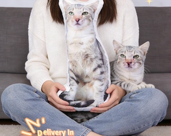 May include: A gray and white cat-shaped pillow is held by a person. The pillow has a realistic image of a cat. A real cat of similar coloring sits nearby. The text "Ship in 48 Hours" and "Delivery In 5-7 Days" are also visible.