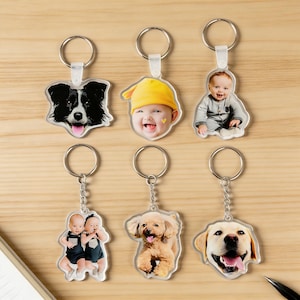 May include: Six personalized keychains with clear acrylic pendants. The pendants feature images of a dog, a baby in a yellow hat, a baby in a gray onesie, two babies, a dog, and a dog. Each keychain has a silver-colored ring and chain.