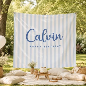 K&ouml;nnte beinhalten: Ein rechteckiger Stoffhintergrund mit vertikalen hellblauen und wei&szlig;en Streifen. Der Name Calvin ist in einer gro&szlig;en, dunkelblauen Schreibschrift gedruckt, darunter steht HAPPY BIRTHDAY in einer kleineren, dunkelblauen serifenlosen Schrift.