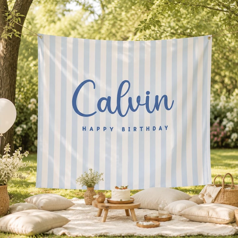 K&ouml;nnte beinhalten: Ein rechteckiger Stoffhintergrund mit vertikalen hellblauen und wei&szlig;en Streifen. Der Name Calvin ist in einer gro&szlig;en, dunkelblauen Schreibschrift gedruckt, darunter steht HAPPY BIRTHDAY in einer kleineren, dunkelblauen serifenlosen Schrift.