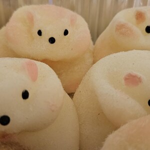 May include: Close-up of several marshmallow treats shaped like small, white bears. Each bear has black eyes and a black nose, with pink accents on the ears and cheeks. The treats are arranged closely together.