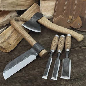 Peut inclure: Ensemble d'outils de menuiserie, comprenant une hache, un grand couteau et trois ciseaux. Les outils ont des manches en bois et des lames en métal. Un étui en cuir est visible en arrière-plan. Les outils sont disposés sur une surface en bois.