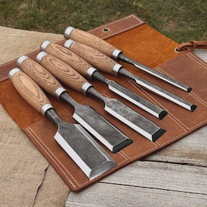 May include: A set of six wood chisels with wooden handles and metal blades, displayed on a brown leather tool roll. The chisels have a variety of blade shapes and sizes, suitable for woodworking projects. The handles are light brown with a wood grain pattern.
