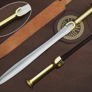 Op de afbeelding: Een zwaard met een gepolijst stalen lemmet en een goudkleurige handgreep. Het zwaard wordt getoond met een bruine leren schede en een decoratieve houten plaat. De handgreep heeft een uniek U-vormig ontwerp.