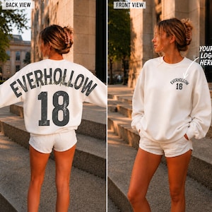 May include: A white long-sleeve sweatshirt featuring the text EVERHOLLOW 18 in a large, distressed dark font on the back. The front displays a smaller version of the same text and number on the left chest area, with an arrow pointing to it.