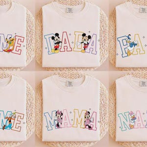K&ouml;nnte beinhalten: Wei&szlig;e T-Shirts mit verschiedenen Disney-Charakter-Designs. Jedes Shirt hat ein anderes Design, darunter Charaktere wie Mickey Mouse, Donald Duck und Pluto, mit Texten wie "NAME", "DADA" und "MAMA" in farbenfrohen Buchstaben.