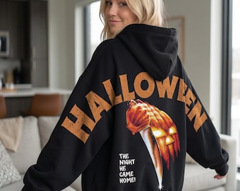 May include: A black hooded sweatshirt featuring a large orange graphic on the back. The text HALLOWEEN arches over a glowing jack-o'-lantern holding a silver knife, with the text THE NIGHT HE CAME HOME printed below the graphic.