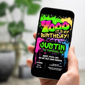 May include: A black smartphone displays a colorful birthday invitation. The text reads "Todd it's my birthday! Justin is turning 12." The invitation features graffiti-style lettering in neon green, pink, and blue. The invitation also includes the date, time, and location.
