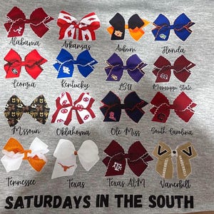 May include: Gray t-shirt featuring various decorative bows, each representing a different college team, with team names below. The phrase "SATURDAYS IN THE SOUTH" is printed at the bottom. Bows are in team colors.