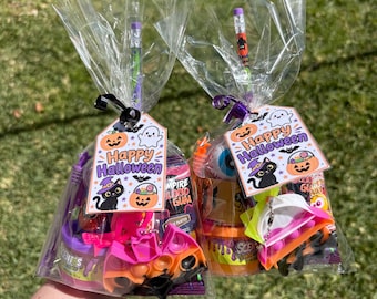 May include: Two clear plastic gift bags filled with Halloween party favors, including orange and purple containers, a bat-shaped fidget toy, a pencil, and a tag with a black cat, pumpkin, and the text Happy Halloween in purple and orange.