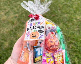May include: A clear plastic treat bag filled with assorted Halloween-themed candies and small toys. A tag attached with a red ribbon features the text Happy Halloween, a pumpkin, a bat, and a spider. The bag contains popping candy, lollipops, and a green bubble wand.