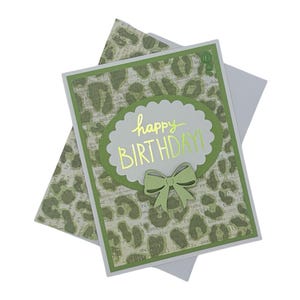 May include: A birthday card with a green and white leopard print design. The card features a scalloped oval with the words "happy BIRTHDAY!" in gold lettering and a green bow. An envelope is included.