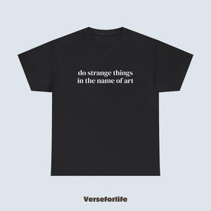 Op de afbeelding: Zwart T-shirt met de witte tekst "do strange things in the name of art". De merknaam "Verseforlife" is in bruin onderaan gedrukt. Het T-shirt heeft een ronde hals.