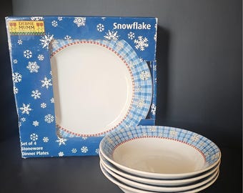 Puede incluir: Un juego de cuatro platos de gres Debbie Mumm Snowflake. El empaque es azul con patrones de copos de nieve blancos y texto. Los platos presentan un centro blanco, un borde a cuadros azules y una fina línea roja con copos de nieve.