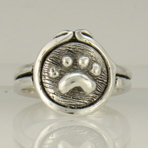 May include: Silver ring with a textured circular design featuring a raised paw print.