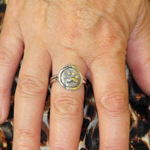 May include: A silver ring with a raised paw print design. The ring is worn on a person's finger.