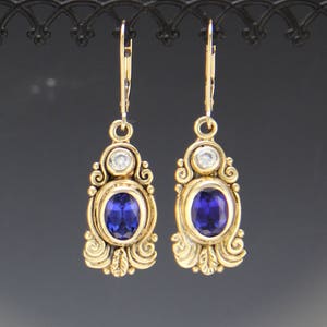 May include: A pair of gold dangle earrings with blue oval gemstones and smaller clear round gemstones. The earrings have a detailed ornate design.