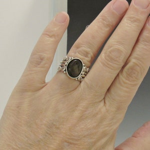 Op de afbeelding: Een zilveren ring met een donkergrijze ovale edelsteen gezet in een swirl-ontwerp.