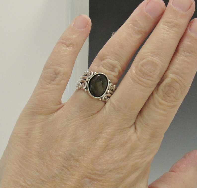 Op de afbeelding: Een zilveren ring met een donkergrijze ovale edelsteen gezet in een swirl-ontwerp.