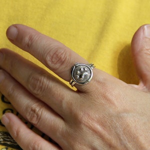 May include: A silver ring with a paw print design. The ring is worn on a person's finger.