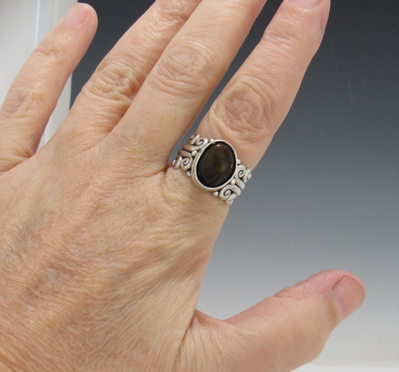 Op de afbeelding: Een zilveren ring met een donkere ovale edelsteen gezet in een wervelend ontwerp.