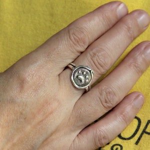 May include: A silver ring with a paw print design. The ring is on a person's finger.