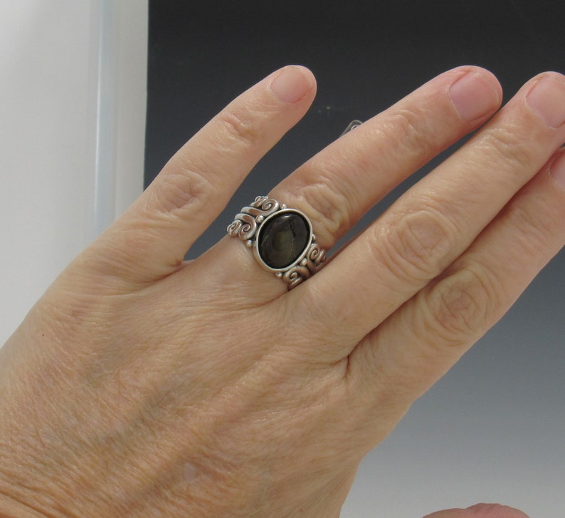 Op de afbeelding: Een zilveren ring met een donkergrijze ovale edelsteen gezet in een wervelend ontwerp.