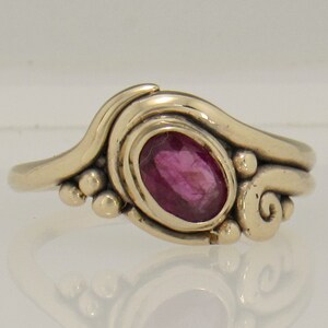 May include: A silver ring with a pink oval gemstone set in a swirling design.