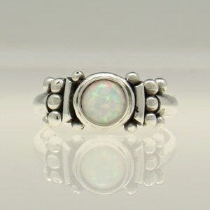 May include: A silver ring with a white opal gemstone set in a bezel setting. The band is decorated with small beads.